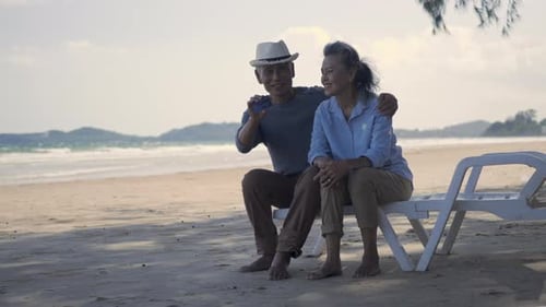 senior couple smile sitting chair beach relaxing outdoors hold and showing credit card payment