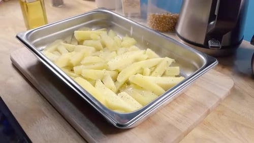 Slow Motion Slider Shot of Seasoning Homemade Oven Fries in a Metal Baking Tray prior to Cooking in