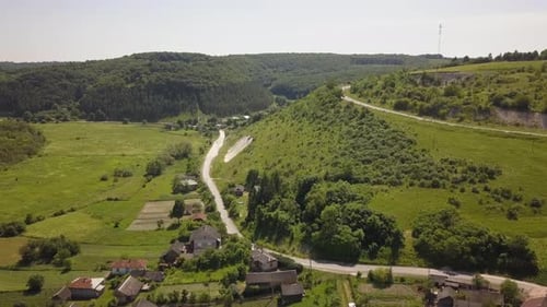 Aerial view of small village with small houses among green trees with farm fields and distant