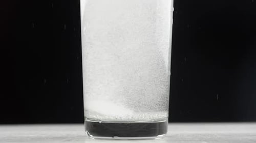 Effervescent aspirin tablet dropping to glass of water. Slow motion fizzy pill falls and dissolves w