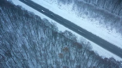 Aerial View of Traffic on the Road Passing Through the Winter Forest in Winter