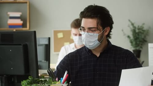 Homme aux cheveux noirs sérieux portant des lunettes de soleil portant un masque médical concentré sur le travail au bureau