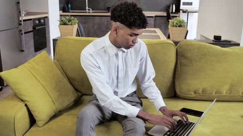 Young Afro Man Freelancer Using Laptop Device on Cozy Couch at Home Office Portrait of Male Working
