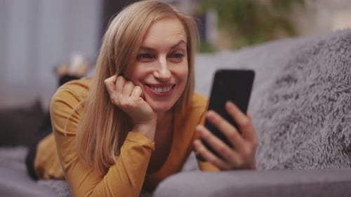 Woman Laughing at Phone While Lying on Couch