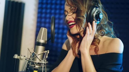 The girl sings into the microphone. A young attractive woman singing in recording studio
