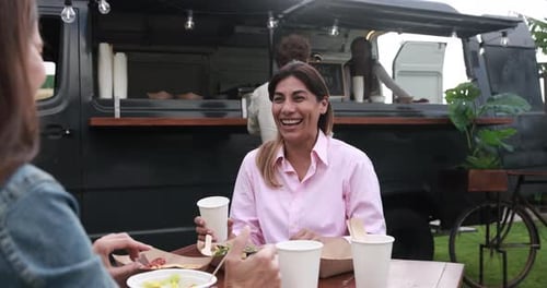 Senior women eating at food truck table outdoor - Mature friends enjoy dinner together