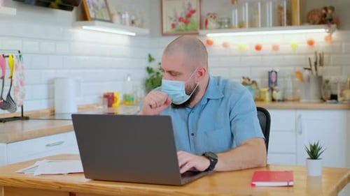 Man Working on Laptop with Mask at Home
