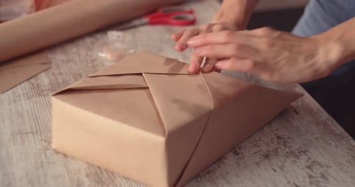 Hands Wrapping Birthday Gift with Brown Paper