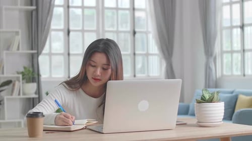 Young Woman Working at Laptop and Writing Notes