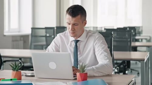 Young Adult Closing Laptop in Brightly Lit Office