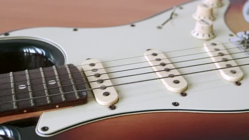 Slide motion of old electric guitar with a fine pattern of guitar strings placed on a wooden floor t