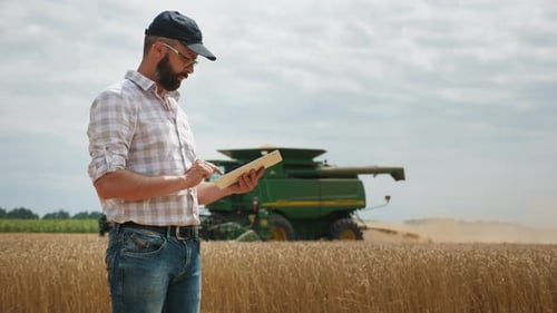 Farmer Using Tablet in Wheat Field with Combine