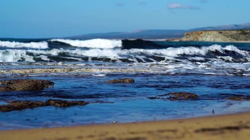Ondas marinhas azuis escuras espirrando na praia arenosa em um dia ensolarado de verão. Águas espumosas do mar Mediterrâneo