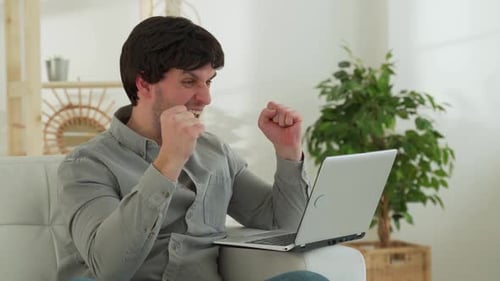 Excited Man Celebrating Success with Laptop at Home