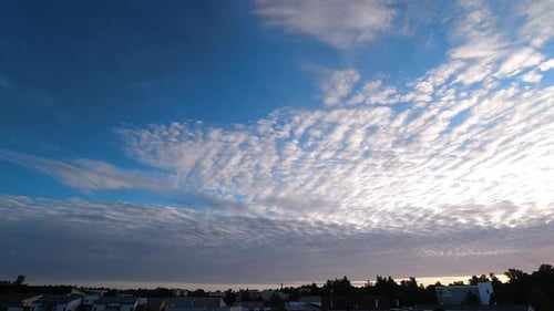 Time lapse of clouds in the sky above city building roofs. Track right shot.