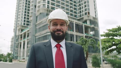 Senior Engineer Planning Manufacture Work in a Business Suit in a White Protective Helmet Checks a