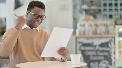 African American Man Celebrating Success While Reading Papers in Cafe