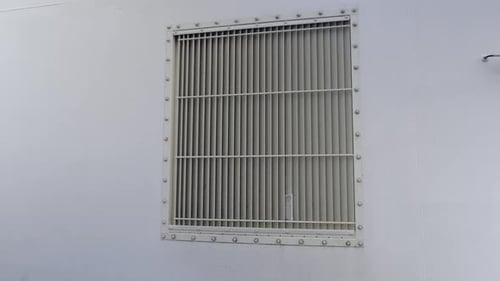 Ventilation system grille in the wall. Square frame with vertical ribs installed on on grey wall of