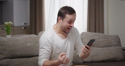 Excited Man Interacts with Smartphone on Sofa