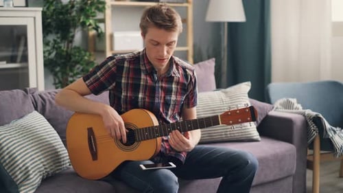 Man Plays Guitar on Sofa Indoors