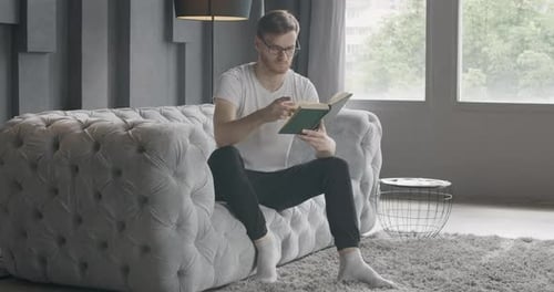 Man Relaxing, Reading Book on Couch Indoors