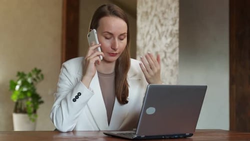 Woman Talks on Phone While Working at Laptop