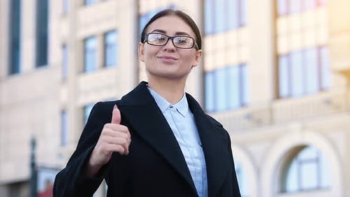 Young Confident Business Woman Shows Thumb Up Sign To Agree. Office Building on the Background