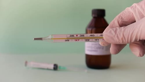 Mão do médico segurando um termômetro clássico de mercúrio em vidro com alta temperatura em Celcius.