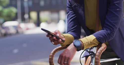 African american woman using smartphone in street leaning on bicycle