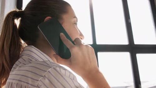 Young Woman Talking on Phone Near Window