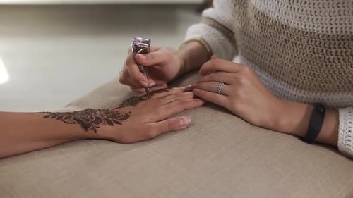 Close Upcshot of a Woman's Hands on a Suntanned Hand Apply a Floral Henna Tattoo