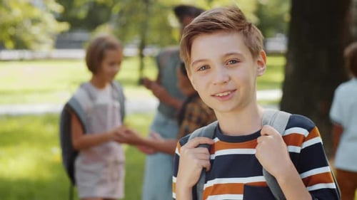 Positive Schoolboy with Backpack Looking at Camera and Smiling in Park