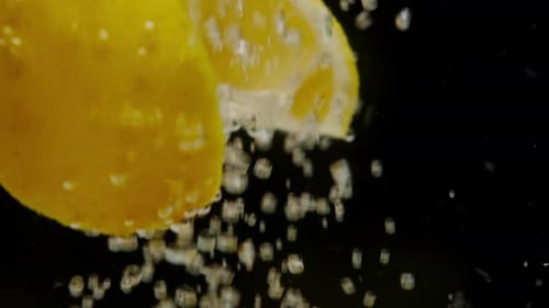 Closeup of Falling Sliced Lemons Into the Sparkling Water on Black Background Making a Cocktail of