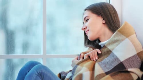 Happy Beautiful Woman Wrap Oneself Up in Warm Plaid Sitting on Window at Winter Weekend