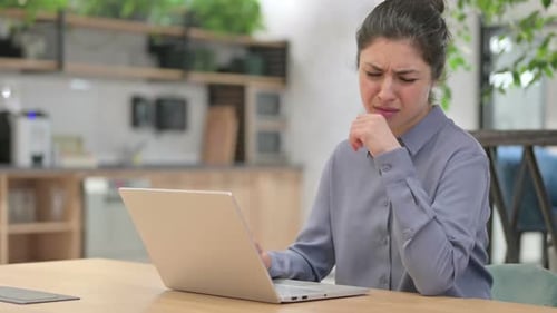 Indische Frau hustet, während sie den Laptop bei der Arbeit benutzt