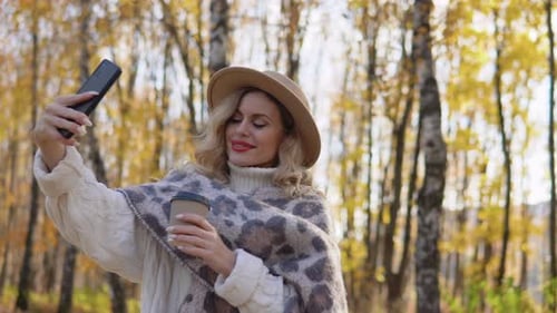 Beautiful Blonde Woman in a Brown Hat Takes a Selfie in the Autumn Park