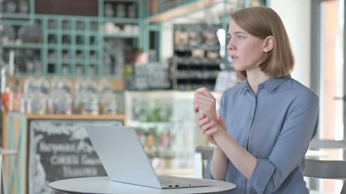 Woman Massages Wrist, Types on Laptop in Cafe