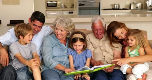 Família extensa olhando para o álbum de fotos juntos no sofá