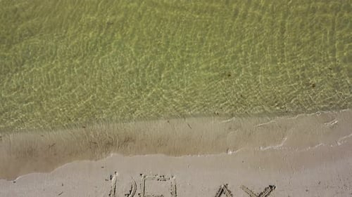 La caméra s'incline de RELAX écrit dans le sable d'une plage à l'horizon montrant l'océan.