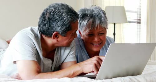 Senior Couple Using Laptop Together on Bed