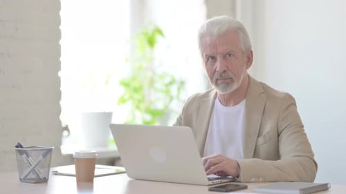 Old Man Looking at Camera While Using Laptop in Office
