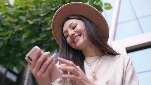 Young Woman with Long Hair and Stylish Hat which Watching Photos on Her Phone