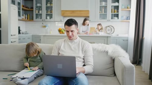 Man Works on Laptop While Child Draws at Home