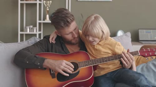 Father Plays Guitar With Child on Lap