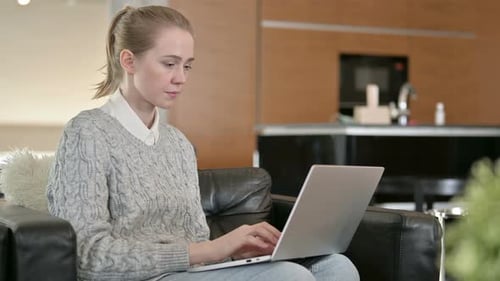 Young Woman Sitting on Sofa and Working on Laptop