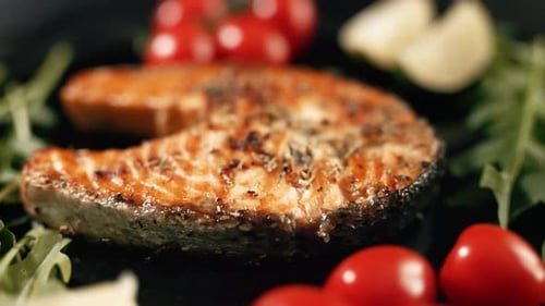 Ein gekochtes Lachssteak mit aromatischen Gewürzen und Gemüse auf einem schwarzen Servierteller
