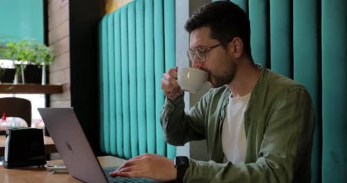 Man in Green Shirt Sitting at Table in Caffe or Coworking Space and Using Laptop Computer
