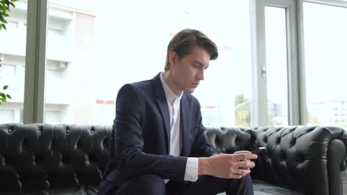 Male millennial professional holding modern smartphone texting message in office