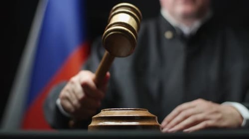 Juez martillando con mazo de madera contra la bandera rusa en la sala del tribunal