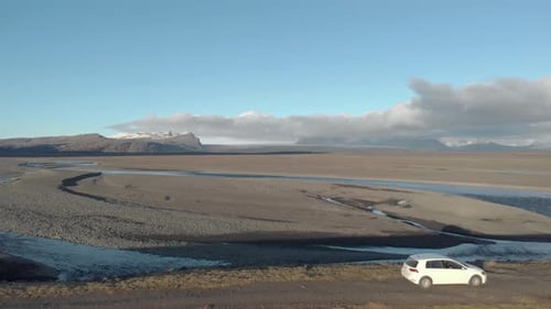 Cinematic Flyover Shot of a Car Parked Along a Glacial River.